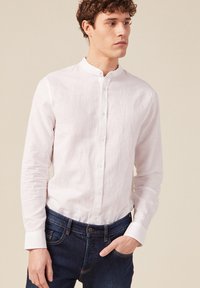 Camicia bianca in lino a maniche lunghe con colletto alla mandarina, chiusura a bottoni e vestibilità comoda, abbinata a jeans in denim scuro.
