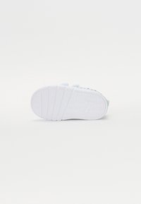 Hvit sneakers med en teksturert gummisåle, med grønne detaljer og et strømlinjeformet design. Lett materiale og minimalistisk stil.