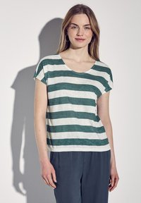 T-shirt a maniche corte a righe verdi e bianche con scollatura a girocollo, realizzato in tessuto leggero. Abbinato a pantaloni scuri, che mostrano una vestibilità rilassata.