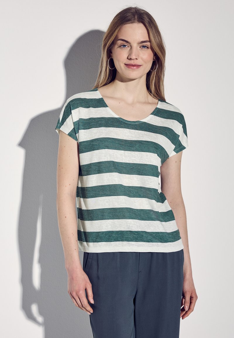 T-shirt a maniche corte a righe verdi e bianche con scollatura a girocollo, realizzato in tessuto leggero. Abbinato a pantaloni scuri, che mostrano una vestibilità rilassata.