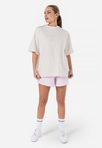 Oversized cream cotton T-shirt with short sleeves and crew neck, paired with light pink ribbed shorts. White sneakers and socks with logo.