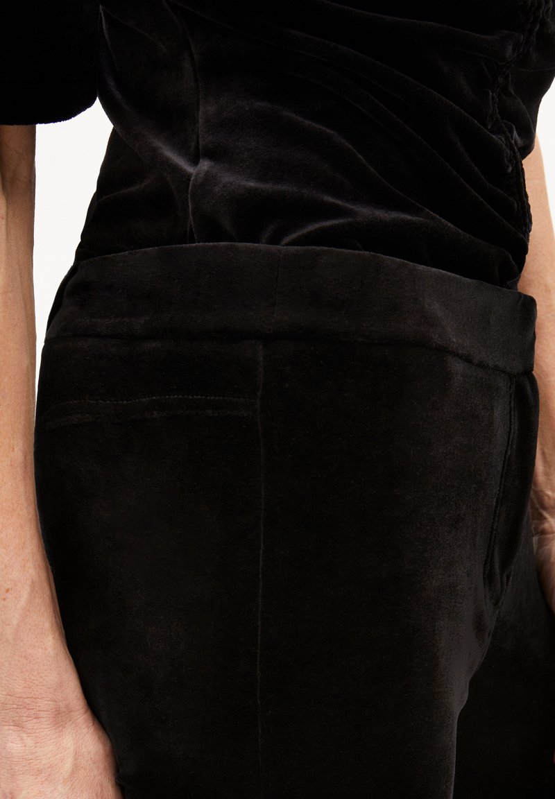 Indumento in velluto nero con una silhouette aderente. Texture liscia e colore uniforme. Cuciture visibili e dettaglio in vita. Senza ulteriori decorazioni.