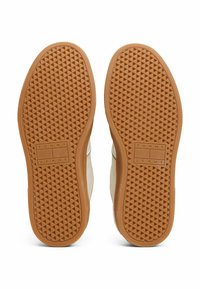 Suole di sneakers in gomma marrone con un motivo a diamante, dotate di un logo rettangolare in rilievo che recita "TOMMY JEANS." Accenti superiori in un morbido beige.