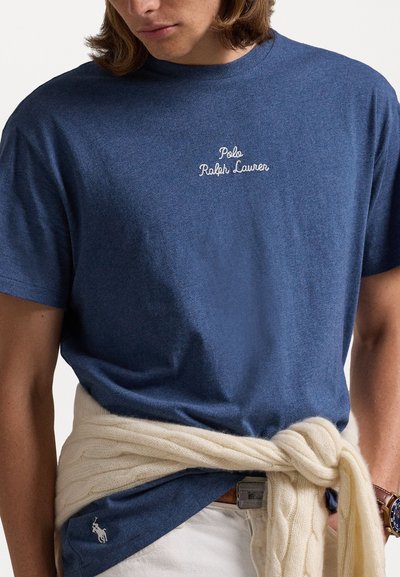 Mörkblå bomull t-shirt med vitt broderat "Polo Ralph Lauren"-logotyp, i kombination med en krämfärgad kabelstickad tröja knuten i midjan.