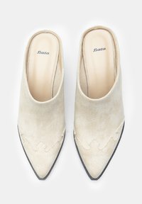 Beige tekstiilidest slip-on jalatsid terava ninaga, millel on kaunistav õmblus ääredel ja sile, lame must tald.