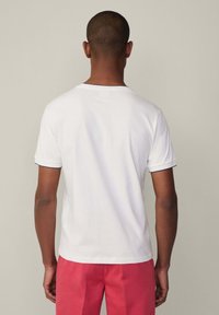 T-shirt bianca a maniche corte con rifiniture blu navy sul colletto e sulle maniche, caratterizzata da una vestibilità regolare e un morbido materiale in cotone.