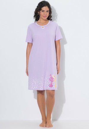 Kobieta o kręconych włosach, ubrana w krótki, lawendowy damski nocny strój w białe kropki z nadrukiem homara przy dole.