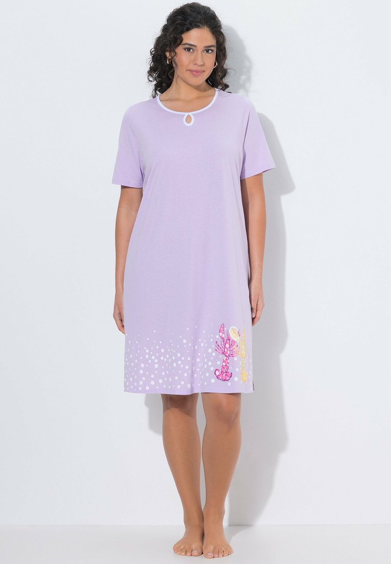 Mujer con cabello rizado que lleva un camisón lavanda de manga corta con lunares blancos y estampado de langosta cerca del dobladillo.