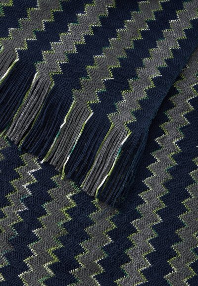 Tissu tricoté avec un motif en zigzag bleu marine, gris et vert, avec des bords frangés sur une surface douce et texturée.