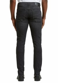 Pantalones vaqueros de mezclilla negra con corte ajustado, que cuentan con bolsillos traseros y una etiqueta de cuero en la cintura. La tela tiene una textura sutil.