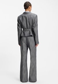 Szürke csíkos, testhezálló blézer peplum szegéllyel, hozzáillő, széles szárú nadrággal párosítva. Az anyag finom textúrával és strukturált sziluettel rendelkezik.