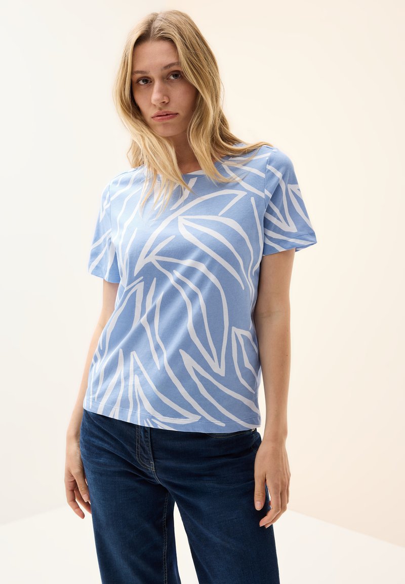 Ljusblå t-shirt med vitt bladmönster, korta ärmar, avslappnad passform, tillverkad av mjukt material, kombinerad med mörkblå jeans.