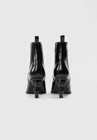 Μαύρα μποτάκια αστραγάλου από δερμάτινο λάκα με τακούνι σε σχήμα γλυπτού. Ο σχεδιασμός διαθέτει κομψή γραμμή, στρογγυλεμένη μύτη και κοντό λουράκι έλξης.