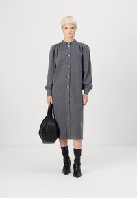 Grå denimkjole med lange puffermer, knapp fram og rund hals. Bært med svarte knelange støvler og en svart veske.