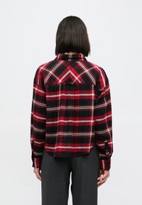 Czerwona i czarna flanelowa koszula w kratę z długimi rękawami, zapinana na guziki z przodu, z przeszyciem na karczku; posiada zaokrąglony dół i dwie tylne kieszenie.
