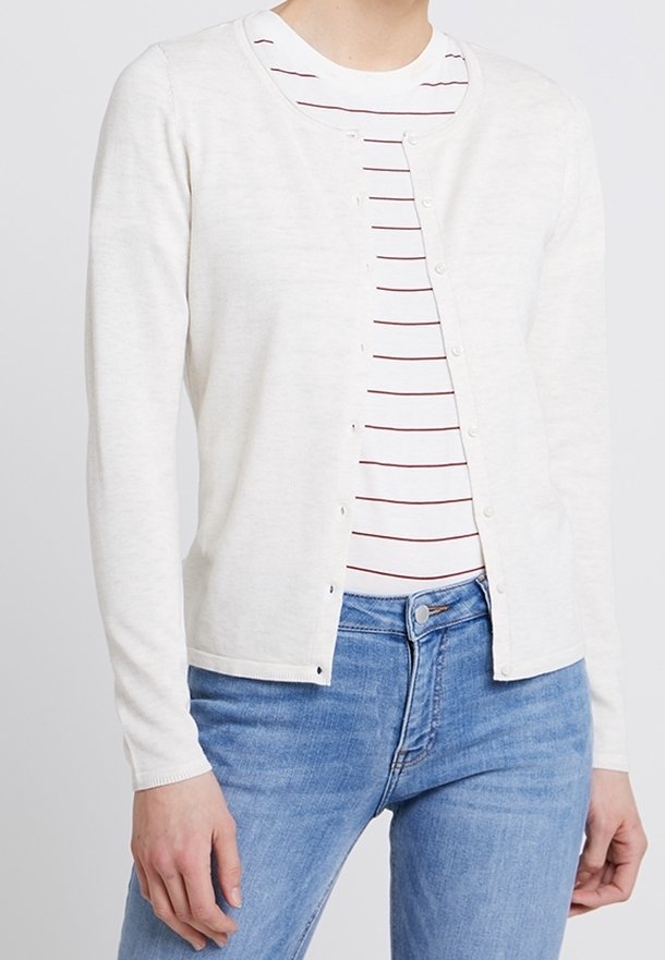Cardigan blanc boutonné porté ouvert sur un t-shirt à col rond blanc et rouge à rayures, associé à un jean bleu clair.