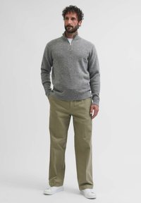 Maglione grigio con zip in maglia, caratterizzato da una texture morbida, abbinato a pantaloni verde oliva chiaro e sneakers bianche. Design semplice e informale.