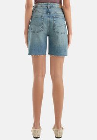 Shorts en denim de couleur bleu clair avec un ourlet effiloché, taille haute et deux poches arrière, portés avec des chaussures beiges. Texture lisse.