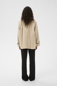 Bézs, túlméretezett dzseki hosszú ujjakkal, fekete gombokkal díszítve az ujján, fekete egyenes szárú nadrággal párosítva.