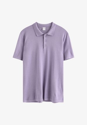 Teenagedreng står med den ene hånd i lommen, iført en lavendelfarvet polo, lyse denimbukser, hvide sokker og gule sneakers.