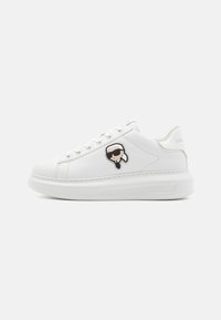 Baskets en cuir blanc avec une texture lisse, dotées d'œillets en métal, d'une semelle épaisse et d'un logo de visage de dessin animé ludique sur le côté.