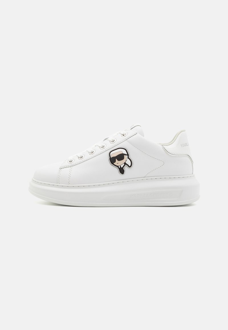 Baskets en cuir blanc avec une texture lisse, dotées d'œillets en métal, d'une semelle épaisse et d'un logo de visage de dessin animé ludique sur le côté.