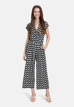 Tuta navy e crema con motivo ondulato, maniche corte, scollatura a V, vita elastica e pantaloni larghi. Modella che indossa sandali dalle tonalità neutre.