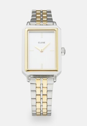 Rechteckige Uhr mit einem weißen Zifferblatt, goldenen Akzenten und einem Armband aus silbernen und goldenen Metallgliedern. Verfügt über minimalistische Markierungen und den Markennamen.