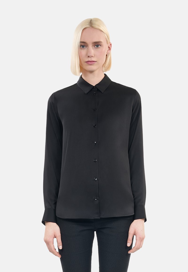 Camicia nera a maniche lunghe in tessuto morbido con chiusura a bottoni, colletto classico e design attillato, abbinata a pantaloni scuri con texture.