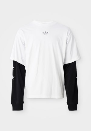 Hvid T-shirt med korte ærmer og sorte lange ærmer. De sorte ærmer har hvide stjernemønstre. Blødt bomuldsstof, afslappet pasform.