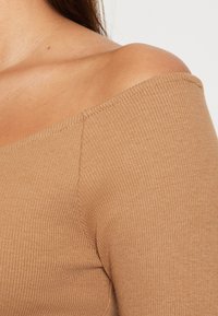 Brown ribbed off-the-shoulder top made of a stretchy material, featuring a fitted design with visible stitching along the neckline and seams.