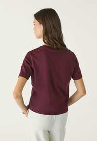 Burgundy lyhythihainen T-paita pehmeästä kankaasta, jossa on pyöreä kaula-aukko ja rento istuvuus, sileä pinta ja yksinkertainen muotoilu.