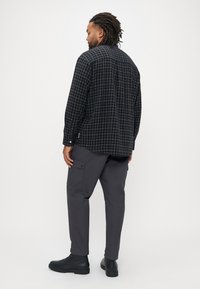 Camisa de manga comprida xadrez a preto e branco, combinada com calças cargo cinza-escuras e botas pretas, vista de costas.