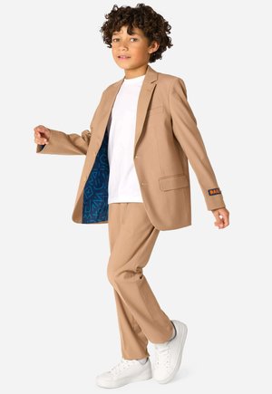 Abito beige con blazer a un bottone, interno a fantasia blu e pantaloni abbinati. Indossato con una camicia bianca e sneakers bianche.