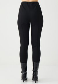 Schwarz hochgeschnittene Leggings mit schlankem Design, aus einem dehnbaren Material hergestellt. Verfügt über dezente Nahtdetails und eine glatte Textur.