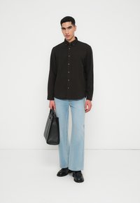 Camisa negra de botones con cuello, jeans de pierna ancha de color azul claro, bolso negro y zapatos negros. Diseño simple con botones metálicos.