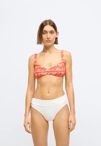 Czerwony top bikini z białym logo w kursywie; konstrukcja z szerokimi ramiączkami. Białe bikini z wysokim stanem dopełnia zestaw.