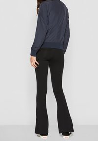 Marinblå bomberjacka med ribbade ärmslut och nederkant, tillsammans med svarta utsvängda leggings och vita sneakers. Slät tyg med minimal struktur.