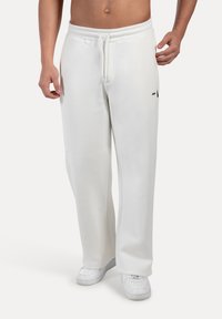 Pantalones de chándal blancos hechos de tela suave, con cintura elástica y cordón, bolsillos laterales y un corte relajado.