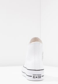 Białe wysokie sneakersy z gładkiego materiału syntetycznego, czarną podeszwą i przeszytymi detalami. Posiadają naszywkę z logo Converse z boku.