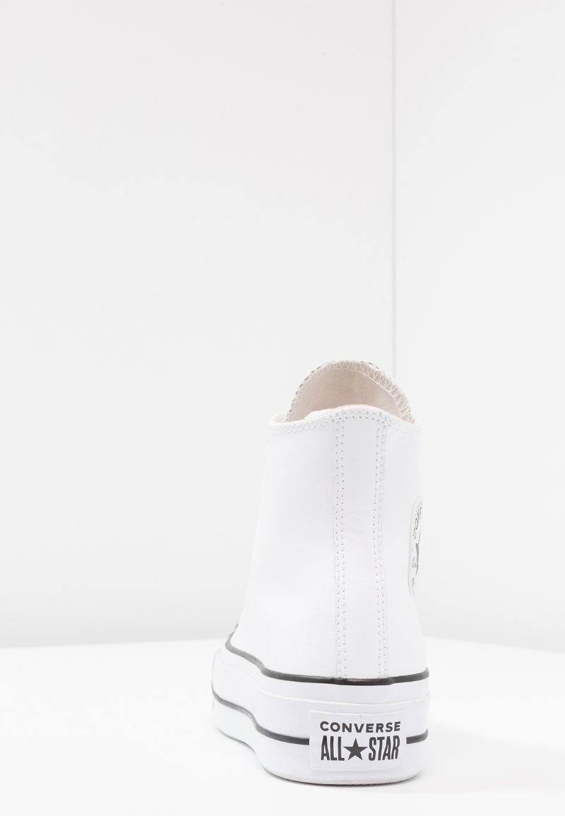 Zapatilla alta blanca de material sintético suave, con suela negra y costuras decorativas. Presenta un parche con el logo de Converse en el lateral.