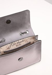 Pieni metallinen hopeinen clutch-laukku, jossa on ketjuhihna, avautuva läppä ja beige sisävuori, jossa on printti "Los Angeles EST. 1981".