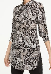 Long-sleeve blouse with a paisley pattern in black, white, and beige. Features a collar and a side slit for ease of movement.