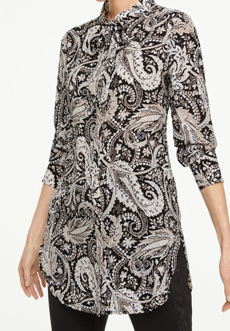 Long-sleeve blouse with a paisley pattern in black, white, and beige. Features a collar and a side slit for ease of movement.