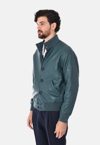 Giubbotto bomber in pelle verde acqua con colletto rialzato, bottoni frontali e tasche laterali. Presenta polsini e orlo a coste per un look aderente.