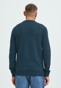 Donker turquoise gebreide trui met lange mouwen, geribbelde manchetten en zoom. De achterkant heeft een eenvoudige, gladde textuur zonder patronen of versieringen.