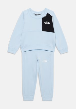 Sweatshirt bleu clair et pantalon assorti avec un panneau noir sur la poitrine. Présente un logo blanc sur la poitrine et la cuisse. Design doux et décontracté.