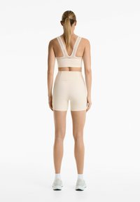 Light beige sports bra with a V-back, featuring decorative cutouts and matching high-waisted shorts. Smooth, stretchy material.