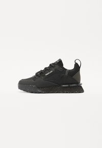 Schwarze Sportschuhe aus einer Kombination von glattem Synthetikmaterial und Mesh, mit einer strukturierten Sohle mit Sprenkeln und schwarzen Schnürsenkeln.