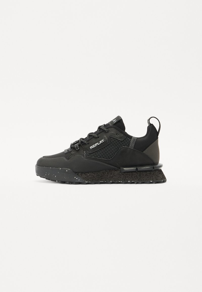 Schwarze Sportschuhe aus einer Kombination von glattem Synthetikmaterial und Mesh, mit einer strukturierten Sohle mit Sprenkeln und schwarzen Schnürsenkeln.